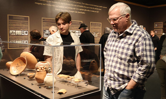 An older man and younger male looking at pottery under glass.